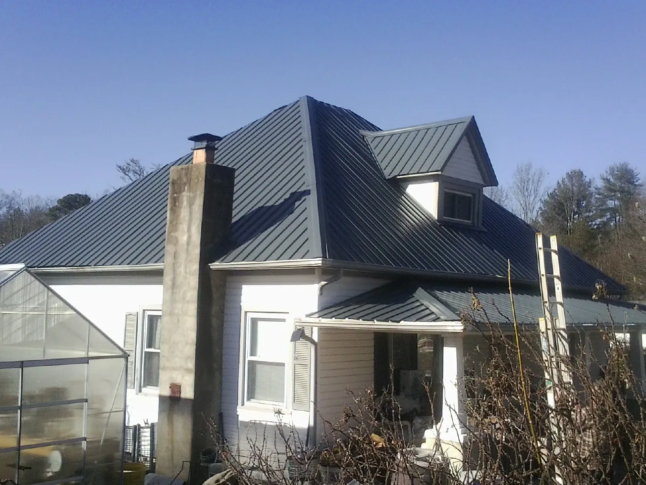 Dark blue standing seam metal roof on a white farmhouse with dormer — Slate & Tile Roof Repair by Roofing Brothers in Cedar Park