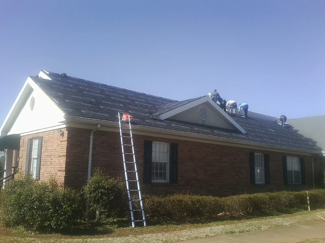 Crew tearing shingles off a brick ranch roof with a ladder set — Emergency Roof Repair work by our crew in Cedar Park