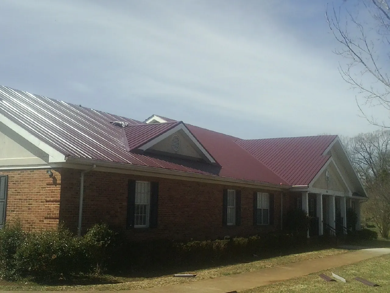 Red metal roof with gabled entries on a long brick building, from a Hail Damage Roof Repair job in Cedar Park