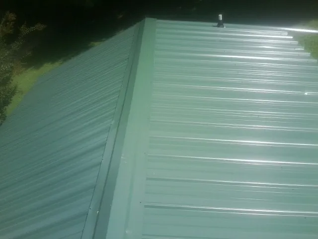 New green metal panels meeting at the ridge of a roof — Flat Roof Repair work by our crew in Cedar Park