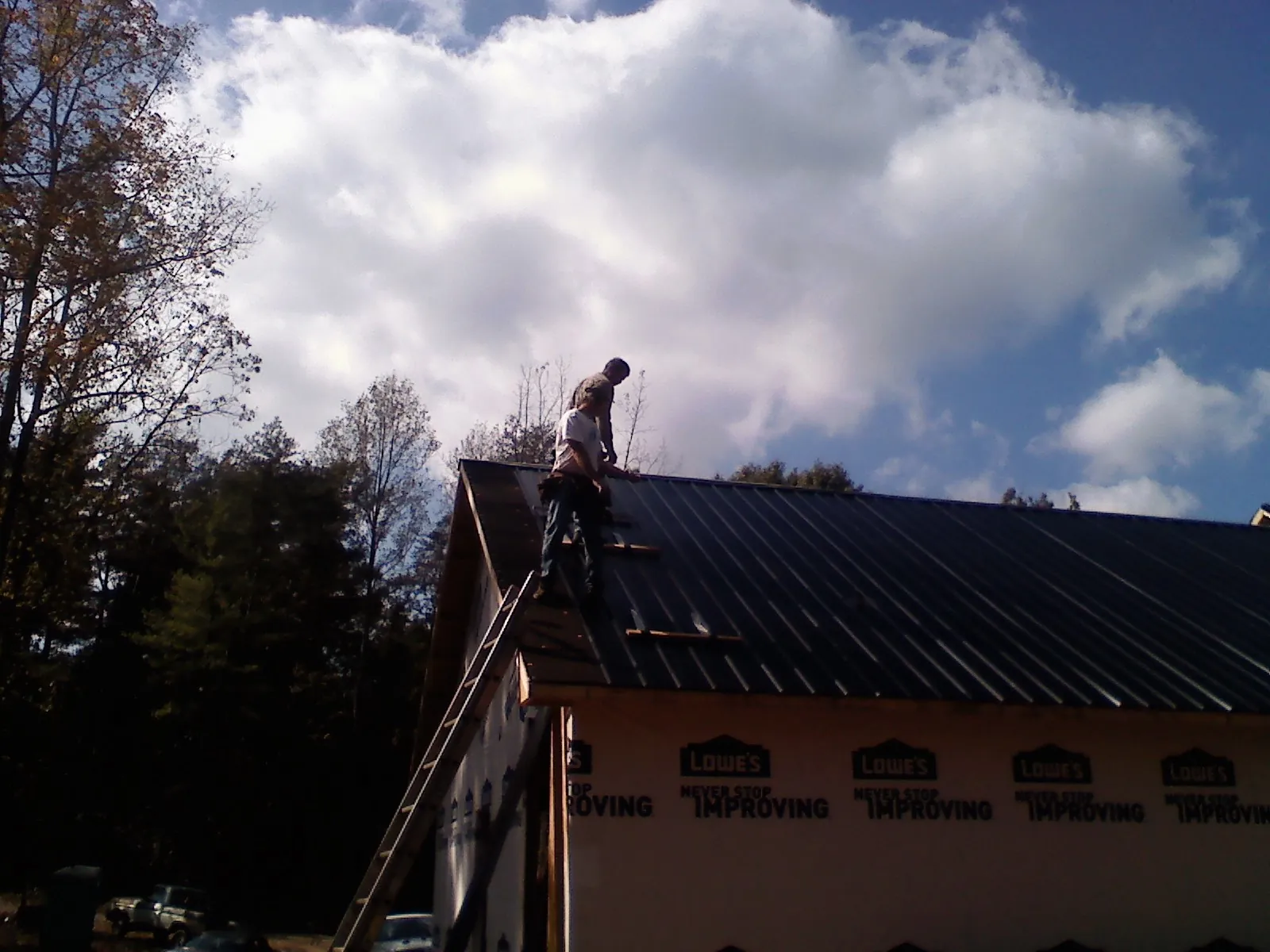 Roofer fastening dark metal panels high against a cloudy sky, from a Roof Inspection job in Cedar Park
